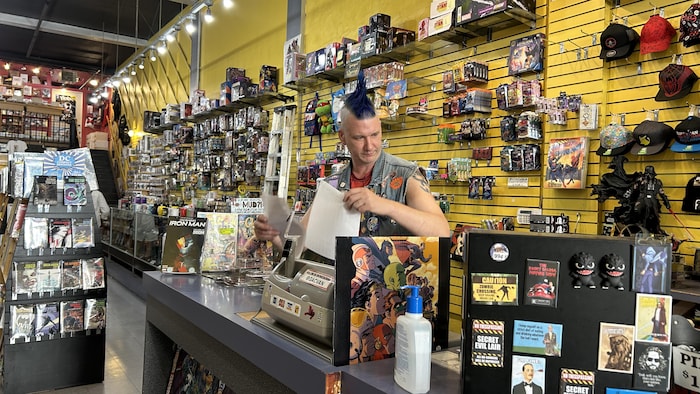 Un homme derrière un comptoir dans un magasin de jeux de carte et de jeux de rôle.