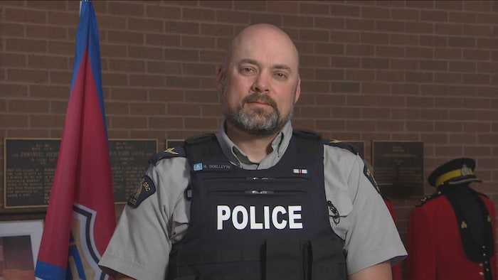 Le caporal Hans Ouellette de la GRC du Nouveau-Brunswick en uniforme devant un mur de brique. 