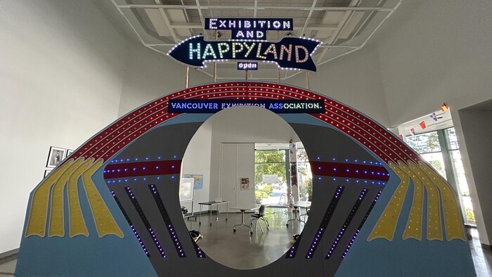 Une grand portail où il est écrit Exposition et Happyland, en anglais. L'entrée du portail démontre ce qui semble être une salle de classe.