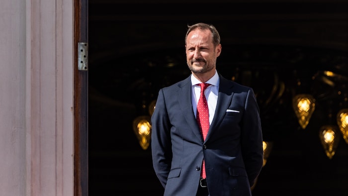 Portrait d'un homme en costume bleu et cravate rouge se tenant sur un balcon.