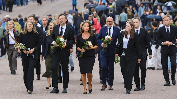 Des hommes et des femmes vêtus de noir portent des bouquets.