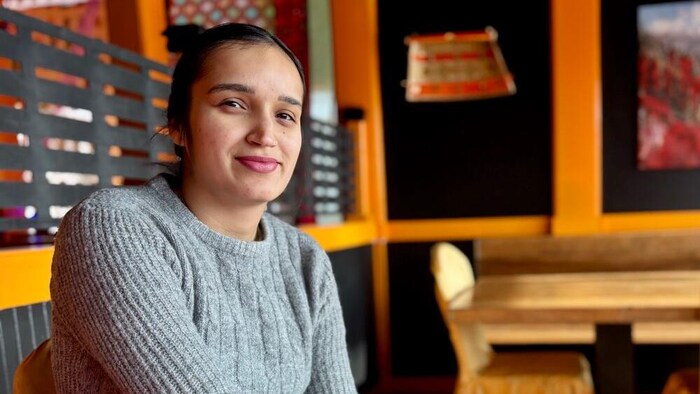 Une femme est assise à une table d'un restaurant indien décoré de couleurs vives. Elle se tourne vers la caméra et sourit.