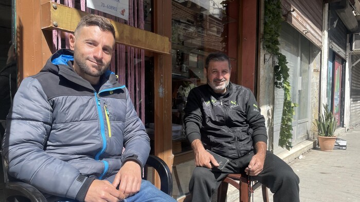 Deux hommes sont assis sur des chaises en plastique sur le trottoir.