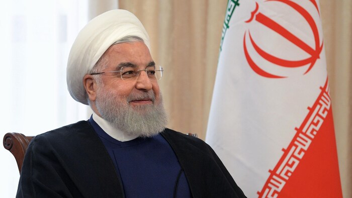 Hassan Rohani,  assis près d'un drapeau iranien.