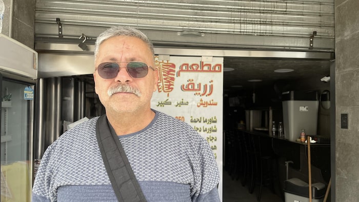 Un homme qui porte des lunettes de soleil est debout devant un petit restaurant.