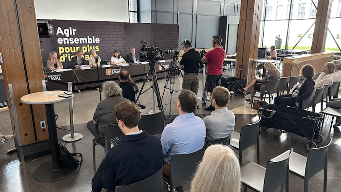 Des gens livrent un point de presse devant une assistance.