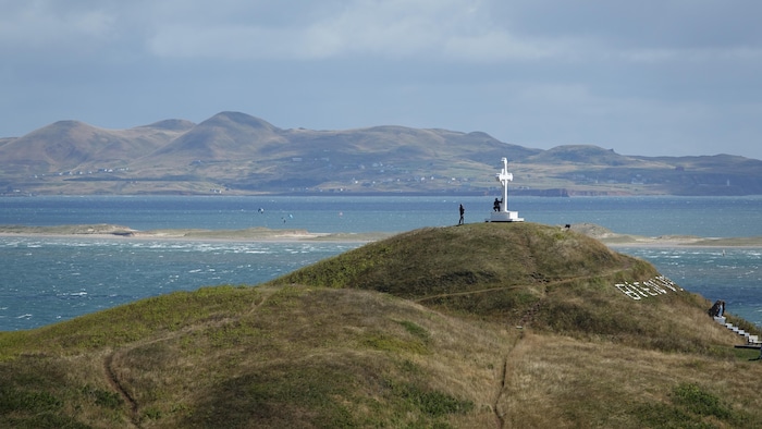 Une croix blanche sur une butte avec l'île d'Entrée en arrière-plan.