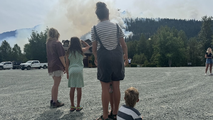 Deux femmes et trois enfants, de dos, observent la fumée qui s'élève d'une colline.
