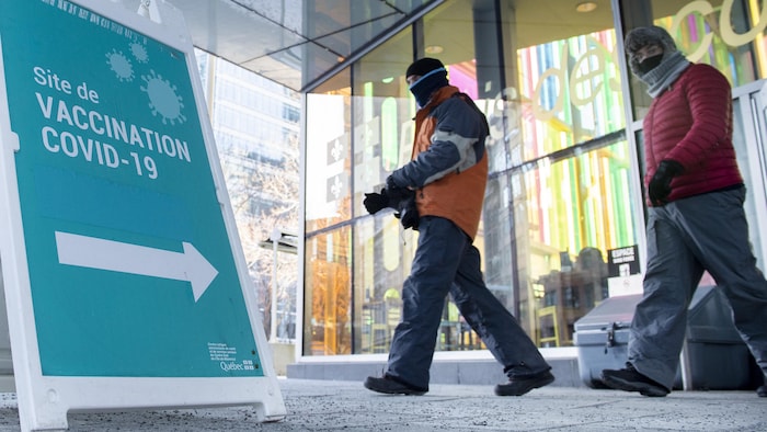 Deux hommes chaudement habillés marchent près d'une pancarte annonçant le site de vaccination du Palais des congrès de Montréal.