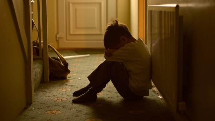 Un enfant triste dans l'entrée d'une maison.