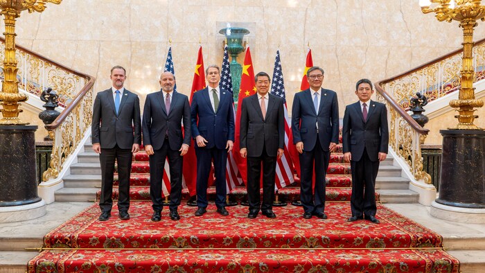 Des hommes posent debout devant des drapeaux chinois et américains.