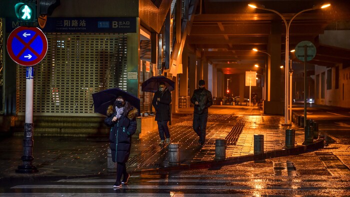 Trois piétons traversent une rue par une nuit pluvieuse.