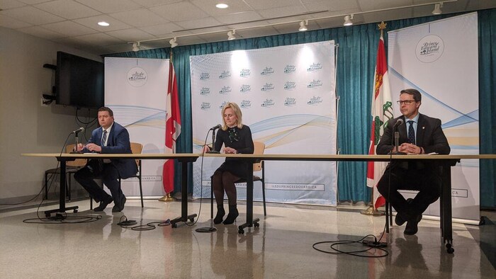 Trois personnes assises à deux mètres de distance les unes des autres pour une conférence de presse.