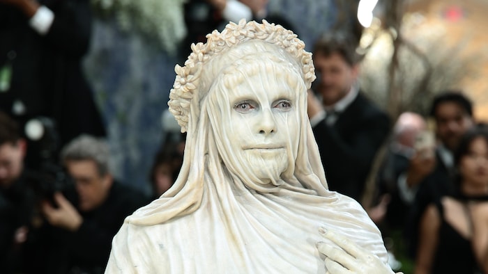 A woman dressed very realistically as a statue poses, motionless, for a photo.