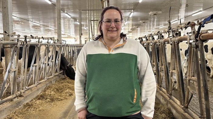 Une femme pose pour la caméra dans une étable avec des vaches de chaque côté.