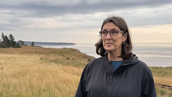 Hélène Boulanger porte une manteau de pluie et se tient sur le bord de l'eau sur l'île d'Anticosti. 