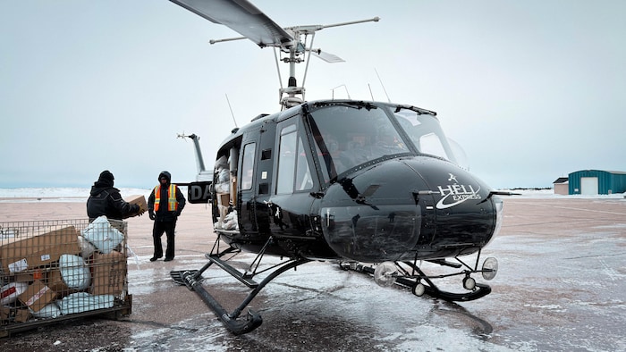 Des hommes placent des boîtes dans un hélicoptère stationné sur le tarmac. 