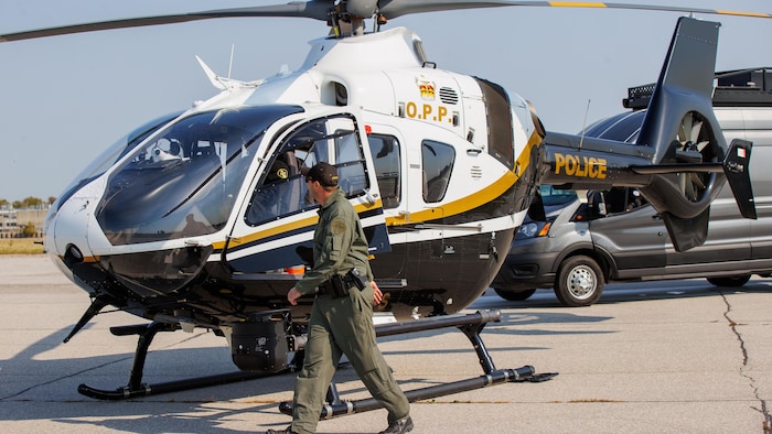 Un policier devant un hélicoptère H135 identifié aux couleurs et au nom de la Police provinciale de l'Ontario.