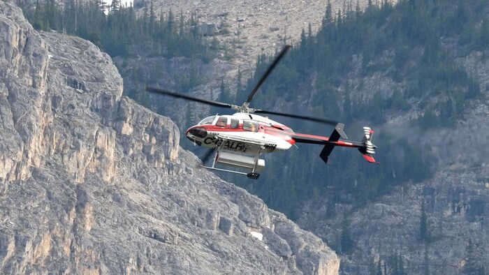 Un hélicoptère au-dessus d'une chaîne de montagnes, dans le parc national Banff, en Alberta, après un éboulement mortel, le 19 juin 2025.