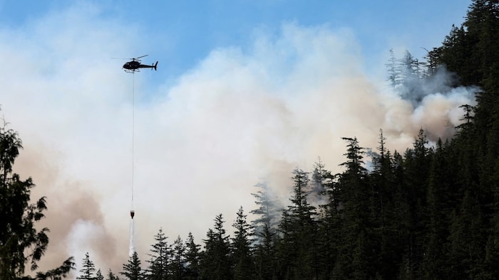 Un hélicoptère entouré de fumée lâche de l'eau sur un feu de forêt à Squamish