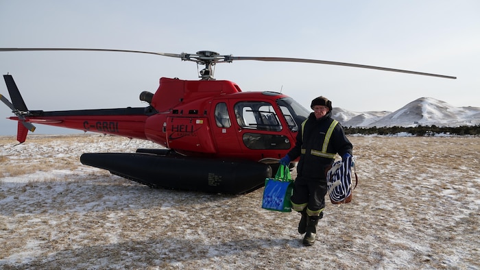 Un employé avec des sacs à la main devant l'hélicoptère.