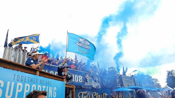 Les spectateurs dans les tribunes décorées de bannières d'un stade extérieur célèbrent en agitant des drapeaux et en faisant monter des colonnes de fumée bleue.
