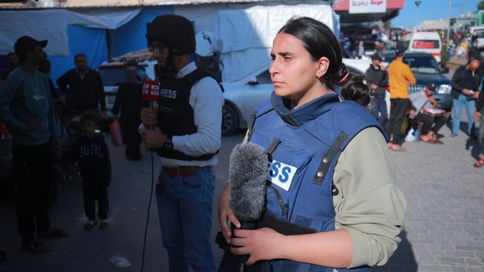Hind Khoudary porte une veste pare-balles identifiée «Presse» et tient un micro.