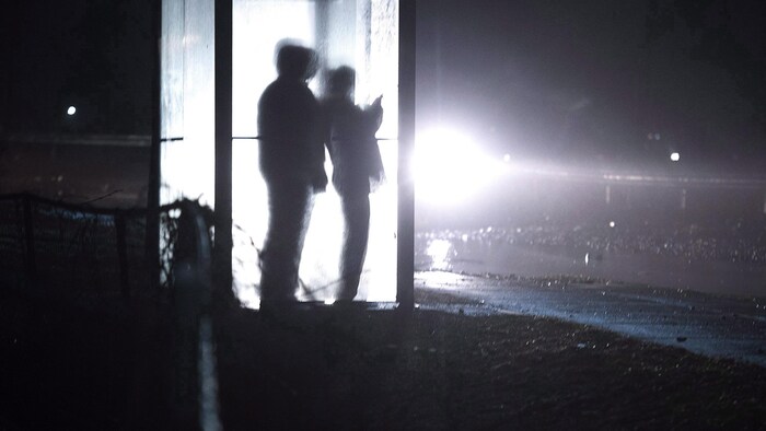 Les silhouettes de deux personnes à travers la vitre d'un abribus, la nuit, en hiver.