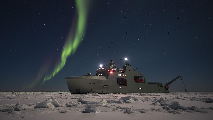 Le bateau NCSM Harry Dewold dans la banquise avec des aurores boréales.