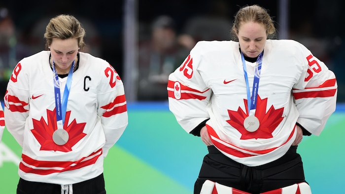 Marie-Philip Poulin et Ann-Renée Desbiens portent leurs médailles d'argent avec la tête baissée.