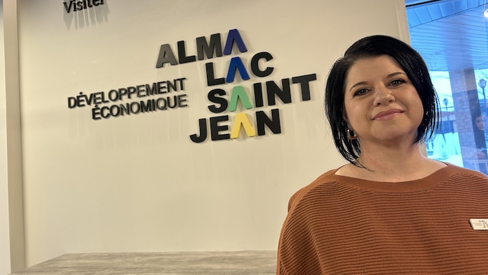 Une dame devant un mur affichant le logo de l'organisme.