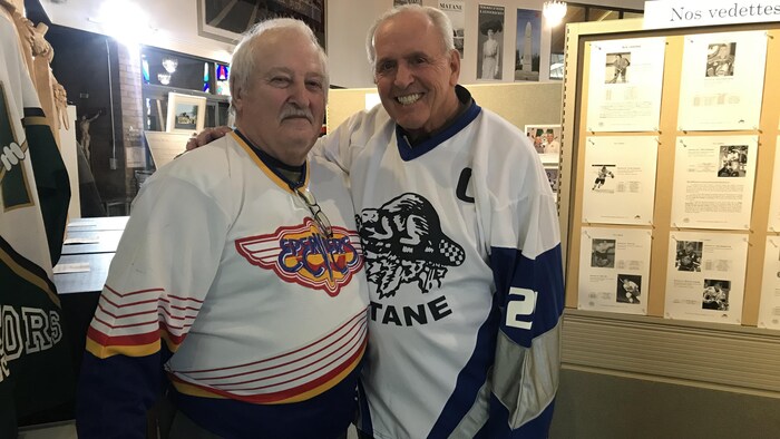 Deux hommes arborant des chandails de hockey regardent l'objectif en souriant.