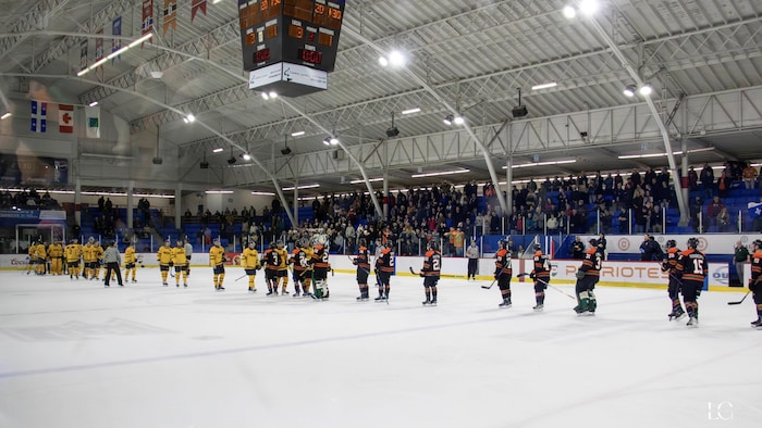 Des joueurs de deux équipes de hockey se donnent la main au centre d’une patinoire.