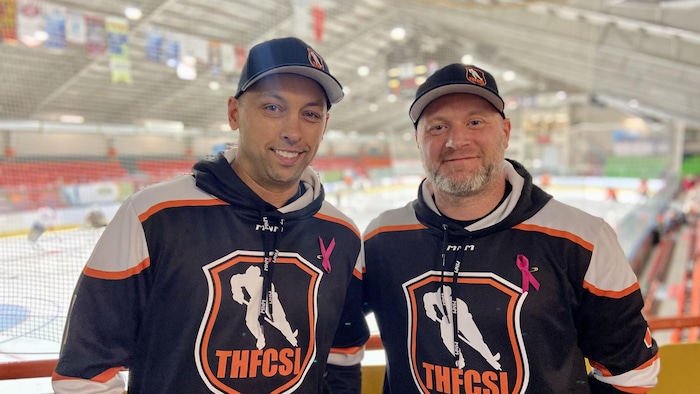 Portant des maillots de hockey, ils sont devant la patinoire dans l'aréna. 