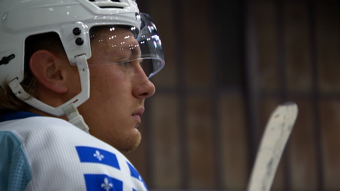 Un jeune homme regarde la glace du banc des joueurs. 
