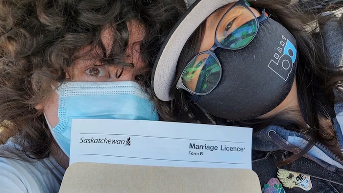 Deux femmes célèbrent l'obtention de leur certificat de mariage, tout en portant des masques.