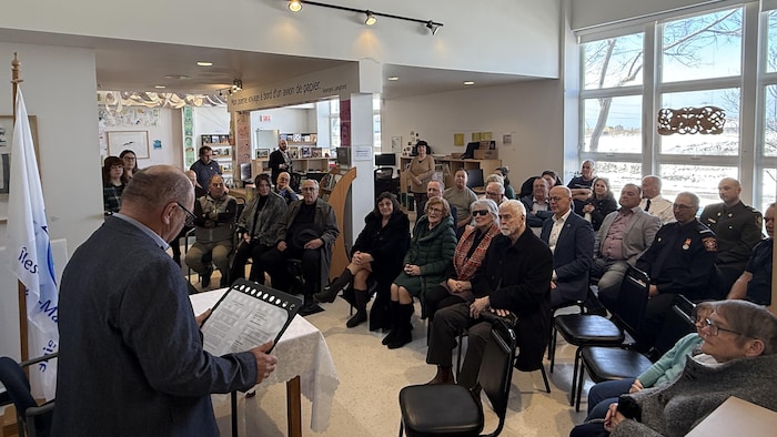 Une trentaine de personnes sont assises et écoutent le maire suppléant des Îles-de-la-Madeleine.