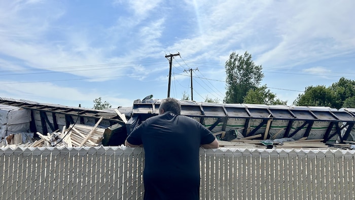 Un citoyen regarde les wagons de bois qui se sont renversés à quelques mètres de la clôture de sa cour.