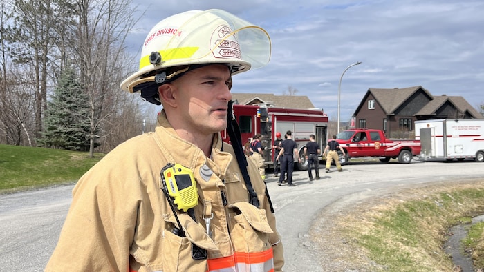 Patrick Hamel regarde sur le côté. Des pompiers travaillent derrière lui.