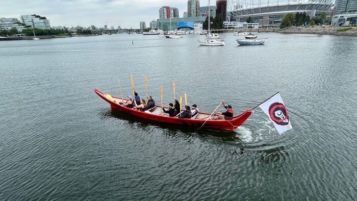 Des Autochtones dans un bateau en bois avec leurs pagaies levées.