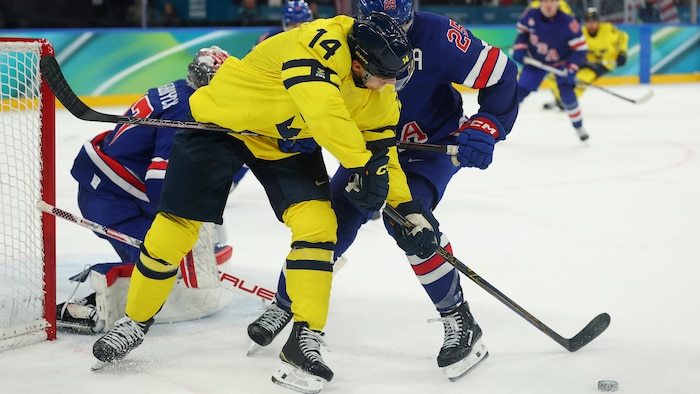 Joel Eriksson, de la Suède, et Charlie McAvoy, des États-Unis, se disputent la rondelle.