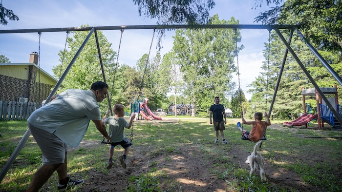 Les deux papas poussent leurs enfants assis sur des balançoires.