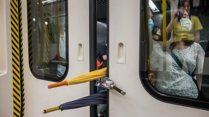 Gros plan de trois parapluies qui bloquent la fermeture d'une porte de métro.