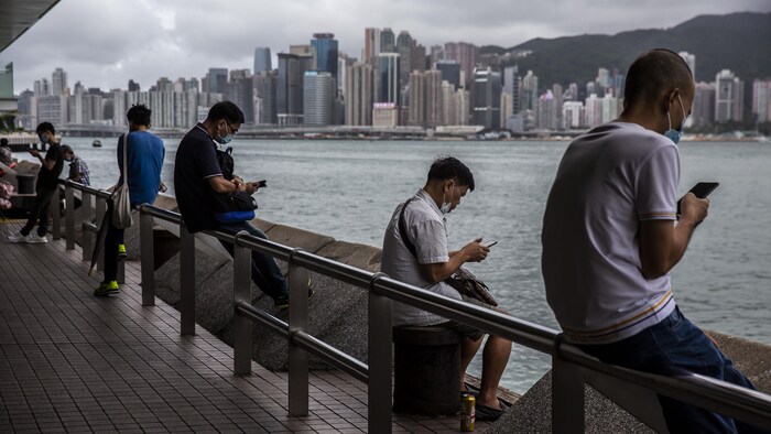 Des Hongkongais consultent leur téléphone intelligent assis sur la promenade Tsim Sha Tsui, à côté du port Victoria de Hong Kong. 
