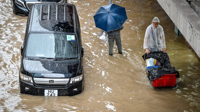 Deux hommes marchent près de deux voitures dans une rue  inondée.