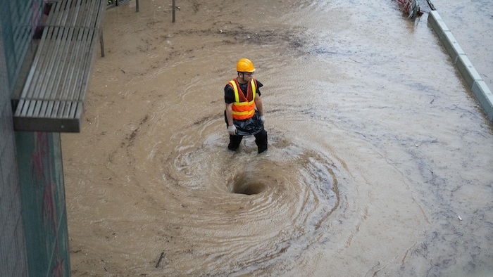 Un travailleur se tient debout devant un tourbillon d'eau dans une rue inondée.