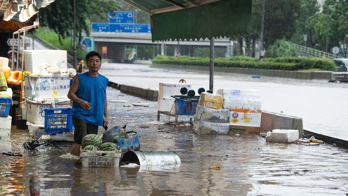 Un homme debout devant une épicerie sur une rue inondée. Des fruits et d'autres débris gisent autour de lui.