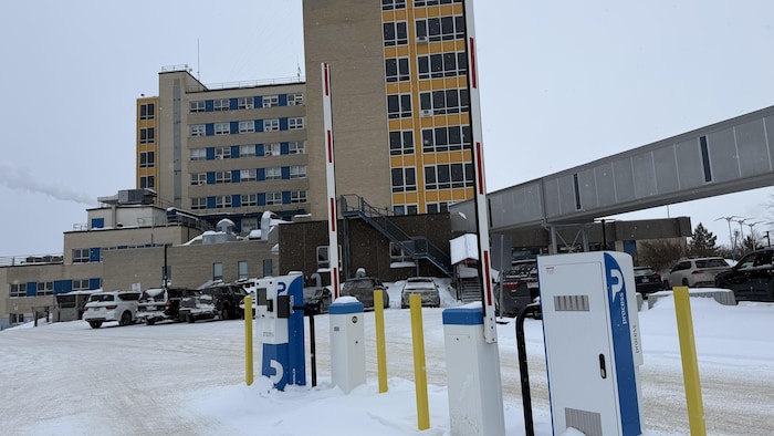 Des barrières levées à une guérite à l'avant-plan et l'hôpital d'Amos à l'arrière-plan.