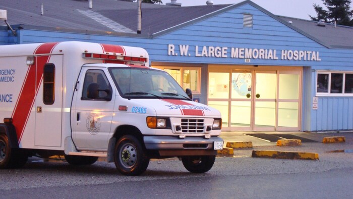À la brunante, une ambulance est stationnée devant l'hôpital qui est illuminé de l'intérieur.