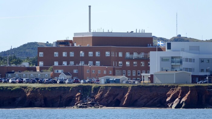 L'hôpital de Cap-aux-Meules, vu de la mer, avec une falaises érodée en avant-plan.                             
